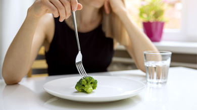 A disgruntled woman contemplating eating a single piece of broccoli